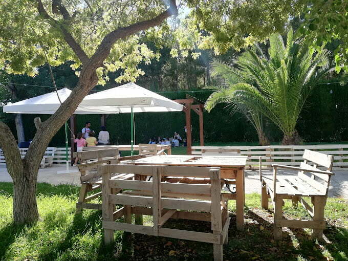 terraza al aire libre en jardín con cesped y mesas de madera con sombrillas blancas